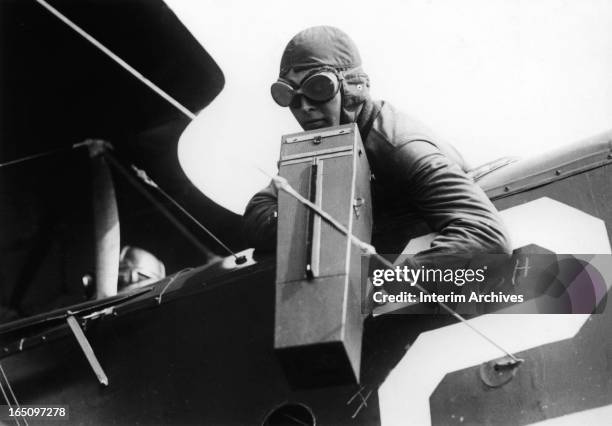 Co-pilot aims a pistol-grip camera over the side of an airplane during World War I, late 1910s.