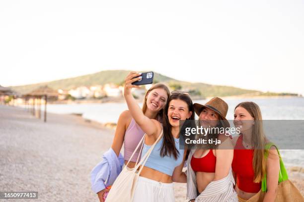 four teenage girls taking a selfie with a mobile phone on the beach in summertime - travel16 stock pictures, royalty-free photos & images