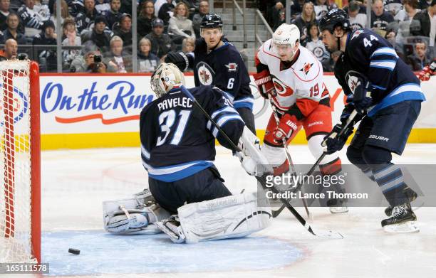 Jiri Tlusty of the Carolina Hurricanes stands between Ron Hainsey and Zach Bogosian of the Winnipeg Jets as they watch the puck slide behind...