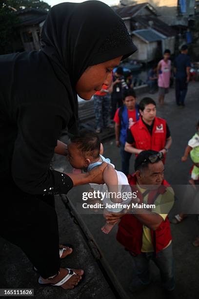 Government social welfare officer lifts a child displaced by continuing armed conflict between the supporters of Philippine Muslim clan Sulu Sultan...