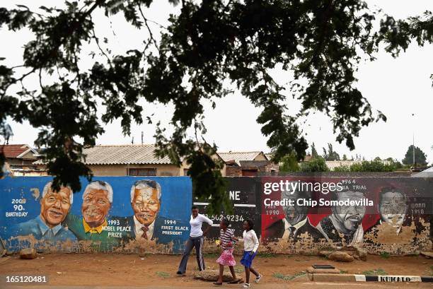 Family walks past a mural depicting former South African President Nelson Mandela during different times in his life near the Regina Mundi Catholic...