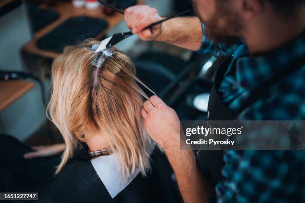 the hairdresser paints the roots of the customer's blond hair with a brush - roots stock pictures, royalty-free photos & images