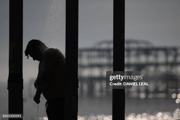 Beachgoer takes a shower in front of the derelict west pier, on the beach at Brighton, on the south coast of England on September 7 as the late...