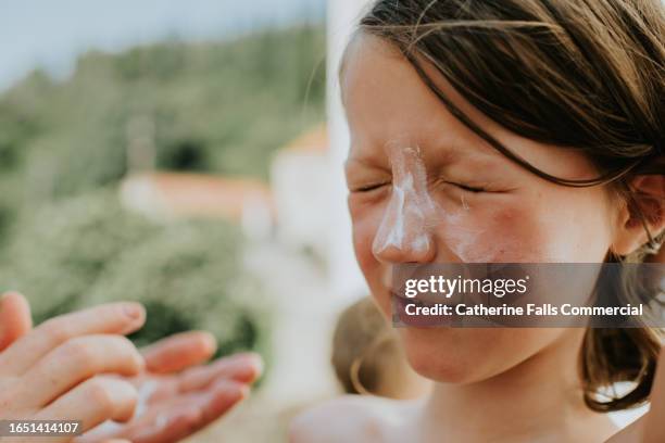 a parent applies sun block lotion to their child's back - parasol persoonlijk accessoire stockfoto's en -beelden