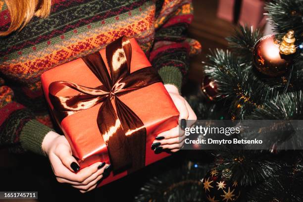 young woman holding christmas present standing by christmas tree at home - julklappar bildbanksfoton och bilder