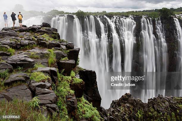 three people looking at victoria falls, zimbabwe, - zambezi river stock pictures, royalty-free photos & images