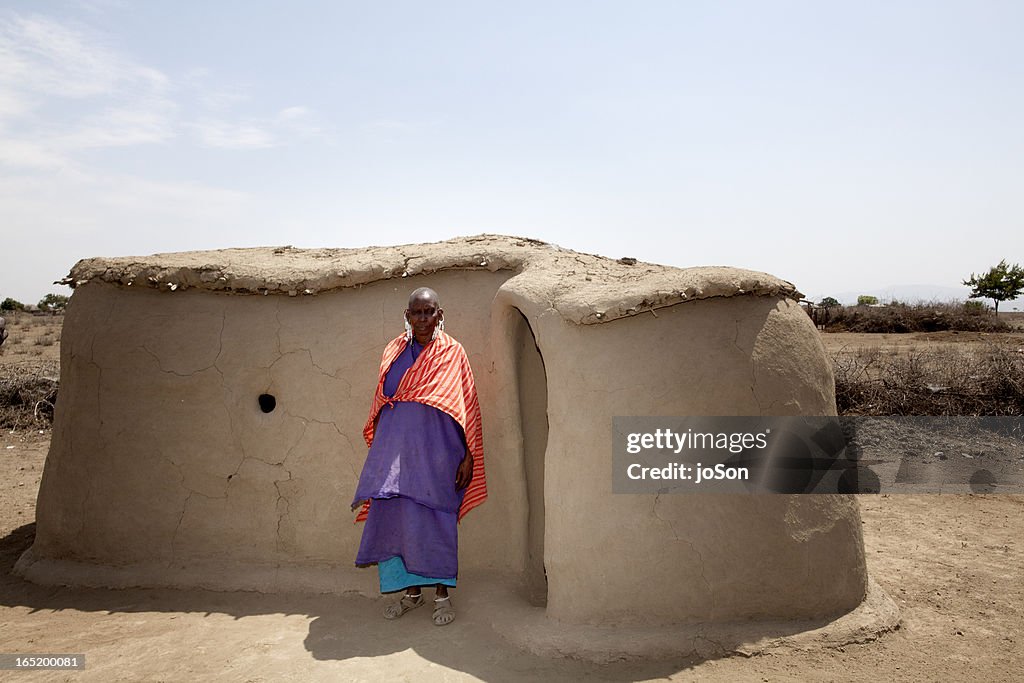Maasai elder stand in front of her home