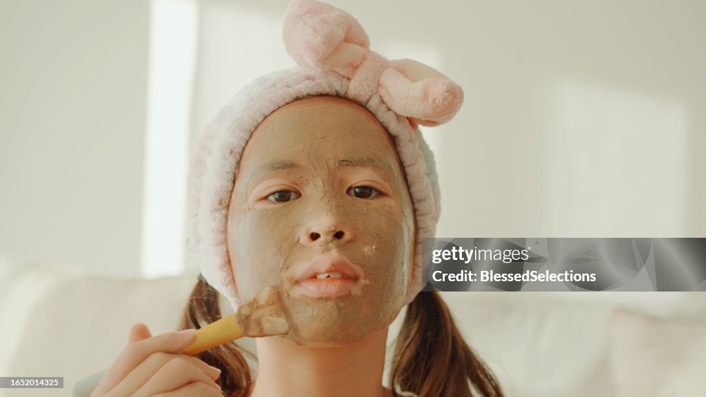 POV of Happy mixed Asian preteen girl applying clay facial mask at home