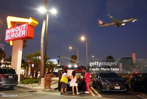 An American Airlines plane lands as people gather in the parking lot of In-N-Out Burger next to Los Angeles International Airport on August 31, 2023...