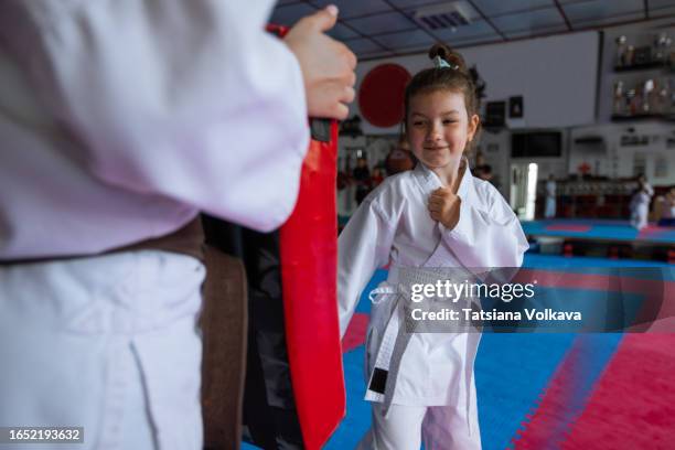 unrecognizable karate coach teaching cute small girl how to punch strike pad during training lesson at martial arts gym - extreem weer stock pictures, royalty-free photos & images