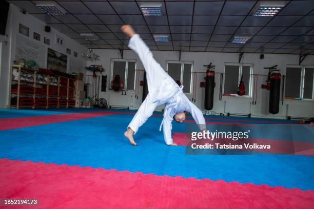 small female karateka in white sports clothing executes cartwheel on gym floor - tatami mat stockfoto's en -beelden