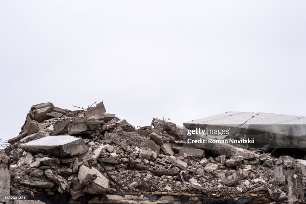 The remains of a destroyed building in the form of a pile of gray concrete debris and construction debris against a gray sky. Background