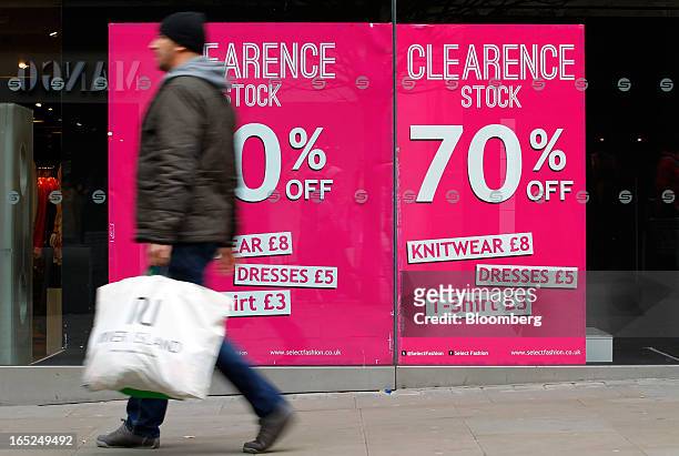 Pedestrian carries a shopping bag past a window advertisement for a stock clearance sale at a Select store in Manchester, U.K., on Monday, April 1,...