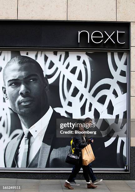 Pedestrians pass an advertisement in the window of a Next Plc store in Manchester, U.K., on Monday, April 1, 2013. U.K. Retail sales unexpectedly...