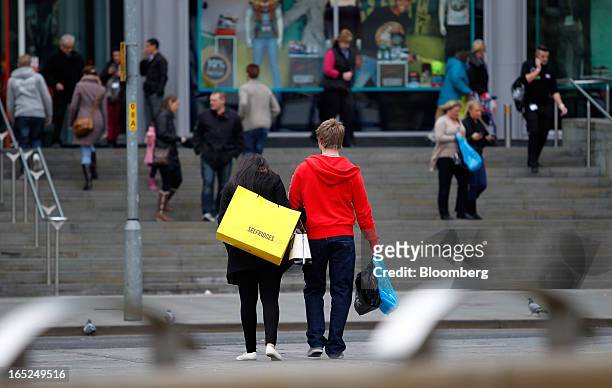 Pedestrian carries a Selfridges & Co.-branded shopping bag, center left, along a street in Manchester, U.K., on Monday, April 1, 2013. U.K. Retail...