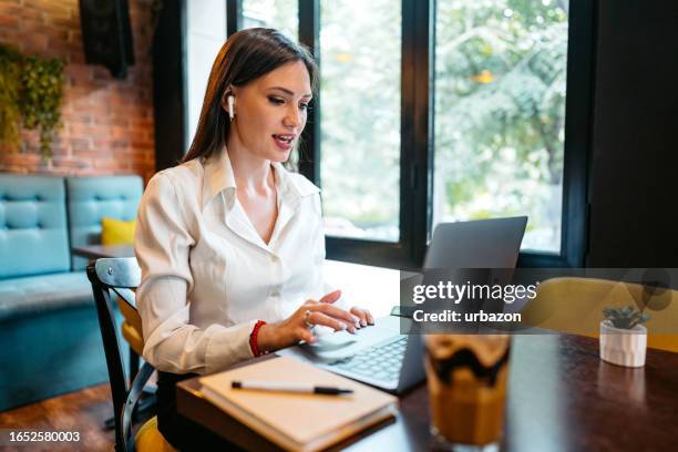 young woman having a video call on the laptop in a café - in ear headphones stock pictures, royalty-free photos & images