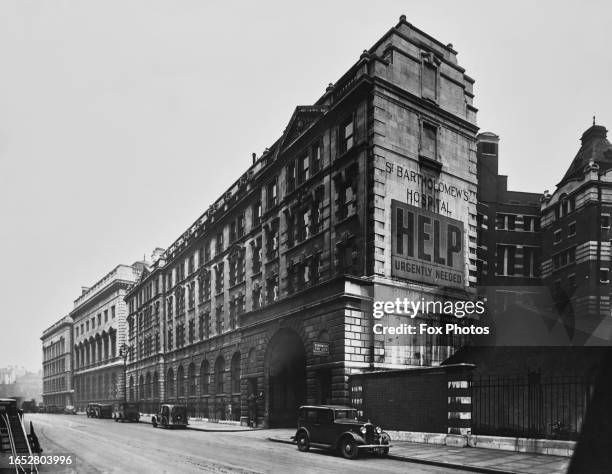 Cars parked along the pavement outside St Bartholomew's Hospital, in a view looking towards Farringdon, in the City of London, England, circa 1935....