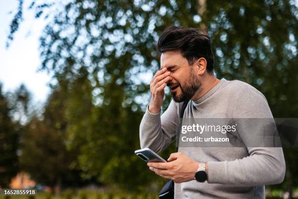 man sneezing while using smartphone outdoors - sneezing stock pictures, royalty-free photos & images