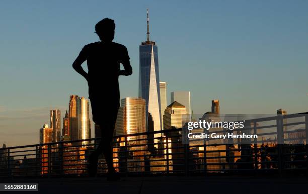 The sun sets on the skyline of lower Manhattan and One World Trade Center in New York City as a person jogs along the Hudson River on August 31 in...