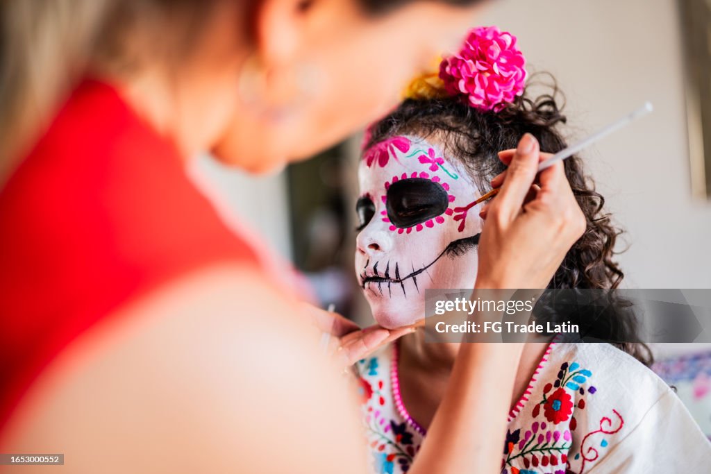 Une mère aide sa fille à se maquiller le visage comme crâne de sucre pour le jour des morts