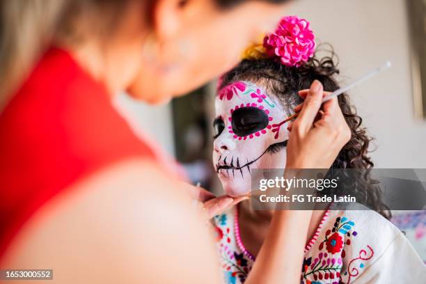 mother helping daughter to get face makeup as a sugar skull for day of the dead - sugar skull stockfoto's en -beelden