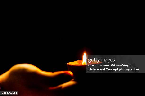 a woman holding an earthen lamp ( diya or deepak) in a dark background during diwali / deepawali festival. - oil lamp stock pictures, royalty-free photos & images