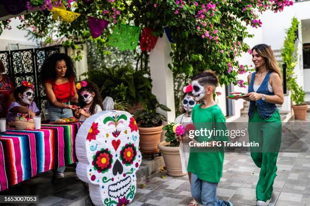 niños y sus madres poniendo decoraciones en una mesa para la celebración del día de la muerte - catrina fotografías e imágenes de stock