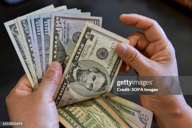 In this photo illustration, a person seen holding 5 and 100 US dollar bills in his hand.