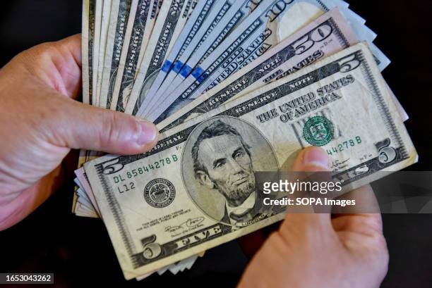 In this photo illustration, a person is seen holding 100 and 5 US dollar bills in his hand.