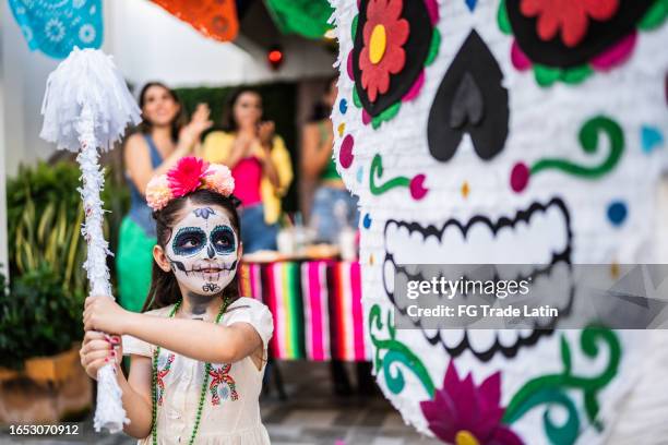 girl hitting piñata during a day of the death celebration - dag-van-de-doden stockfoto's en -beelden