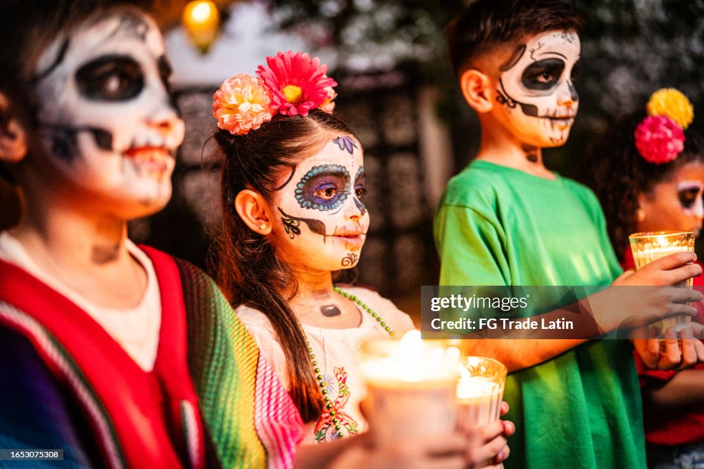 Niños con calavera de azúcar pintada en la cara sosteniendo velas durante la celebración del día de muertos