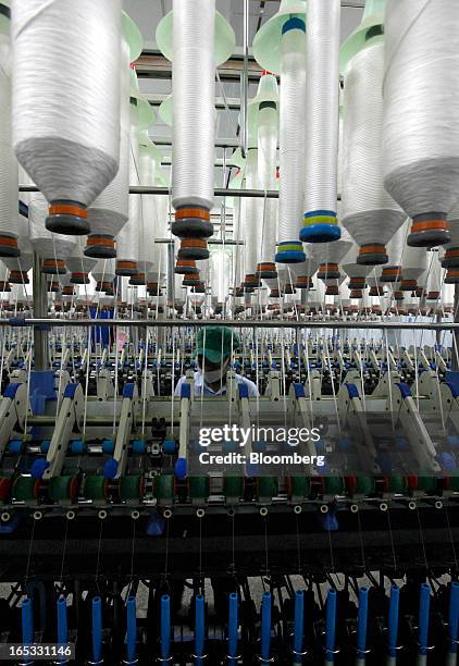 Spools of yarn run through spinning machines as a worker monitors operations in the spinning area at a PT Sri Rejeki Isman factory in Sukoharjo,...