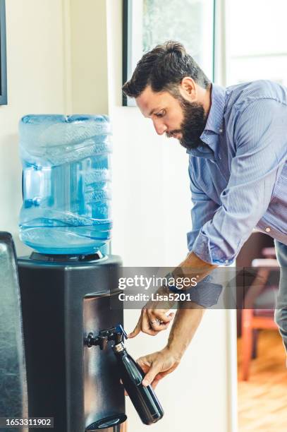 man refills his reusable water bottle at a water cooler in an office - reusable water bottle office stock pictures, royalty-free photos & images