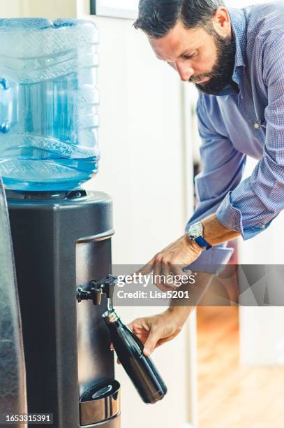 man refills his reusable water bottle at a water cooler in an office - reusable water bottle office stock pictures, royalty-free photos & images