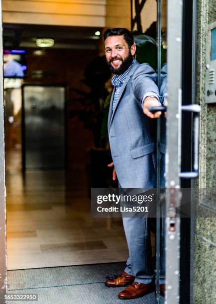 uomo d'affari educato di bell'aspetto in giacca e cravatta tiene una porta aperta in una zona del centro città - aprire foto e immagini stock