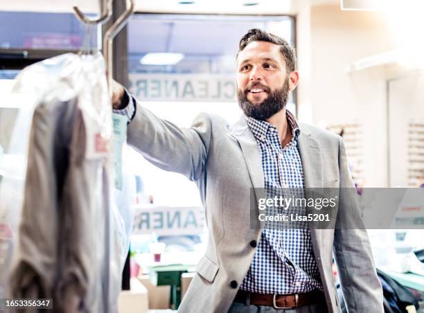 businessman in a small shop picking up his dry cleaning - dry cleaning bag stock pictures, royalty-free photos & images