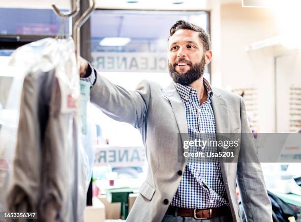 businessman in a small shop picking up his dry cleaning - dry cleaning shop stock pictures, royalty-free photos & images