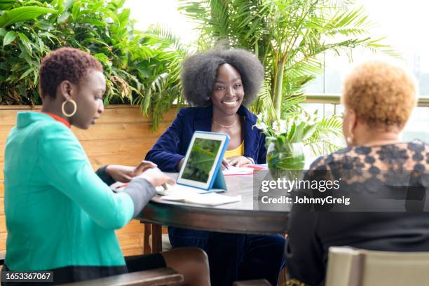 african businesswomen meeting in sunny atrium - round table discussion women stock pictures, royalty-free photos & images