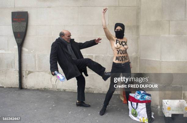 Man kicks a topless activist of the Ukrainian feminist movement Femen as she raises her fist to protest against Islamists in front of the Great...