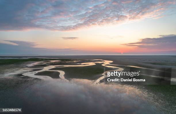 tidal channels on sand plain during colorful sunset above the sea - mar de wadden fotografías e imágenes de stock