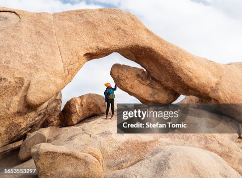 Woman is standing under a large rock in Joshua Tree National Park in Southeastern California Woman is standing under a large rock in Joshua Tree National Park in Southeastern California