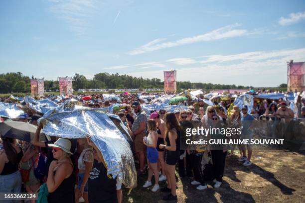 People protect themselves from the heat under the survival blanket as they attend the concert of the US American pop-rock band Imagine Dragons at the...