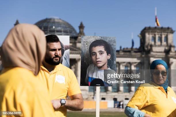 People standing in front of a 50 meters long dinner table showing portraits of orphans in front of the Reichstag in a charity push called "Meals for...