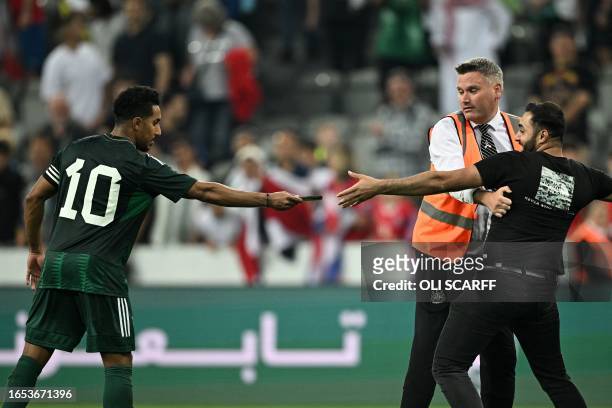 Saudi Arabia's midfielder Salem al-Dawsari returns the phone of a pitch invader who wanted to take a selfie with the player before being stopped by...