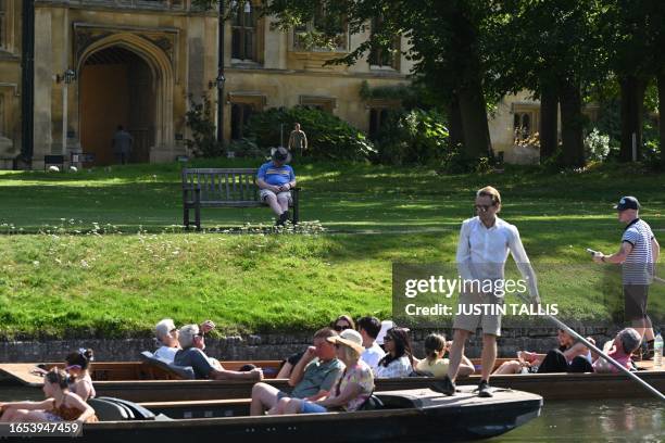 Man sleeps on a bench in front of the Wren Library, part of Trinity College, as people punt past on the River Cam in Cambridge, north of London on...