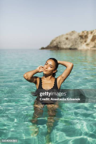 beautiful multiracial woman in black swimsuit with long hair enjoying clear transparent ocean. - mid adult women stock pictures, royalty-free photos & images