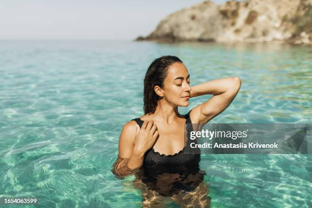 beautiful multiracial woman in black swimsuit with long hair enjoying clear transparent ocean. - mid adult women stock pictures, royalty-free photos & images