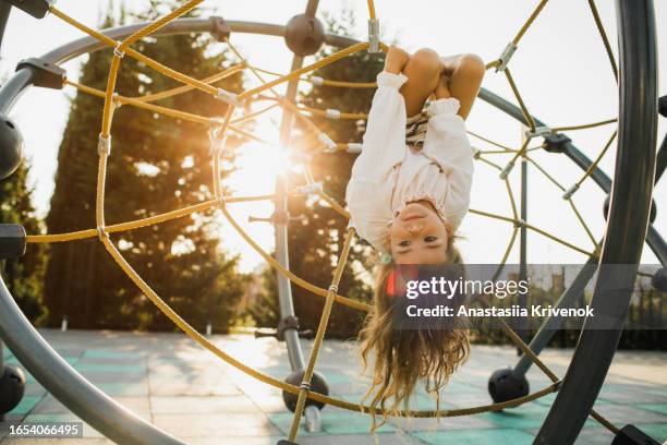 pretty little girl upside down on rope web on outdoor playground. - tau stock-fotos und bilder