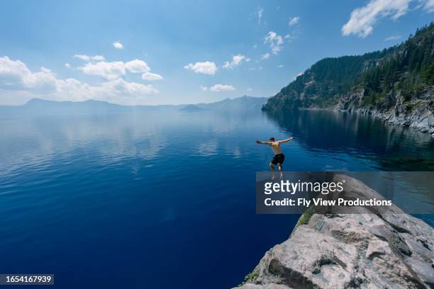 man jumping into crater lake on sunny summer day - jumping into water stock pictures, royalty-free photos & images