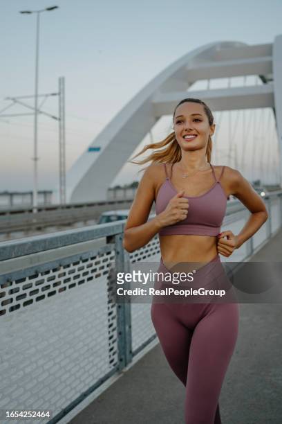 energetic young woman sprints across a scenic bridge - mobility exercise stock pictures, royalty-free photos & images